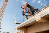 一名佩戴安全設備的人員正在向正在建造的建築物的木樑上鑽孔。.