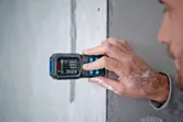 A person uses a laser measure to record distances on a concrete wall.