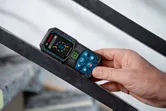 A person uses a laser measure to check the angle of a metal beam.