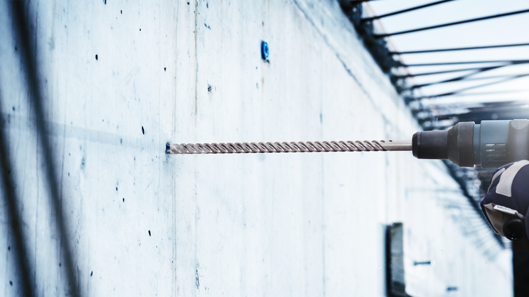 配戴安全設備的人員使用旋轉錘在混凝土牆上鑽孔。