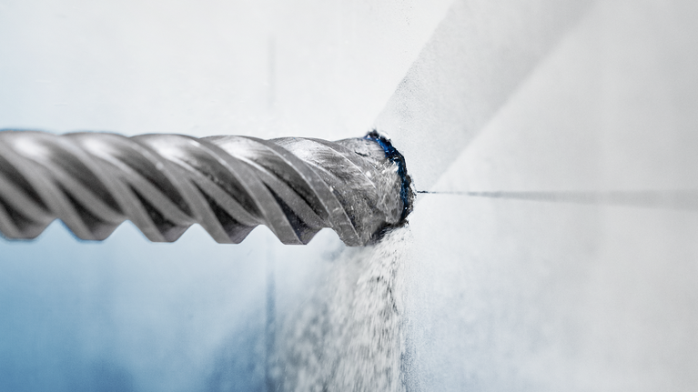 鑽頭鑽入混凝土牆，產生灰塵。