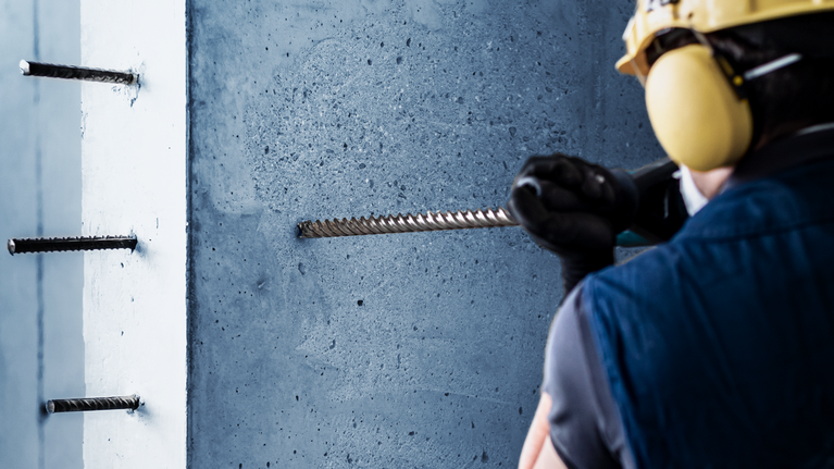 佩戴安全設備的人員在混凝土中鑽孔以安裝鋼筋。