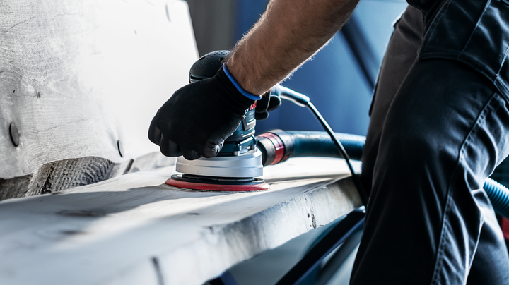 配戴安全設備的人員使用電動砂光機打磨木板。