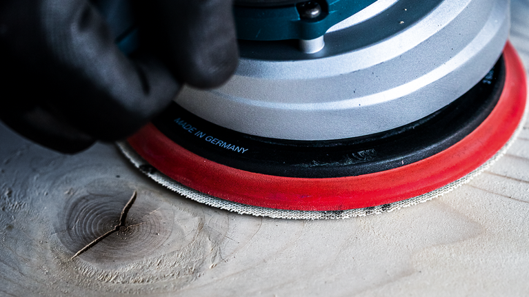 一名配戴安全設備的人員正在使用電動工具打磨木質表面。