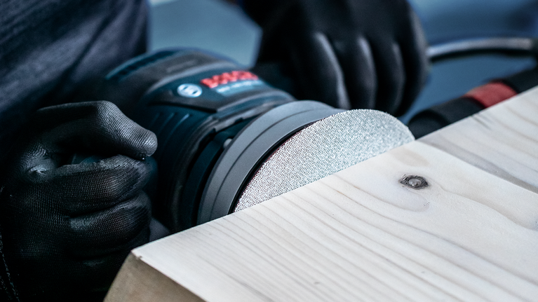 配戴安全設備的人員使用電動工具打磨木質表面。