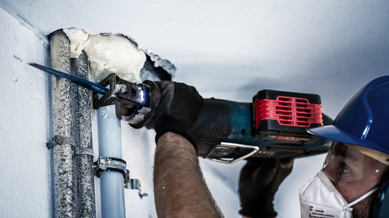 一名配戴安全設備的人員使用往復鋸切割金屬管路。