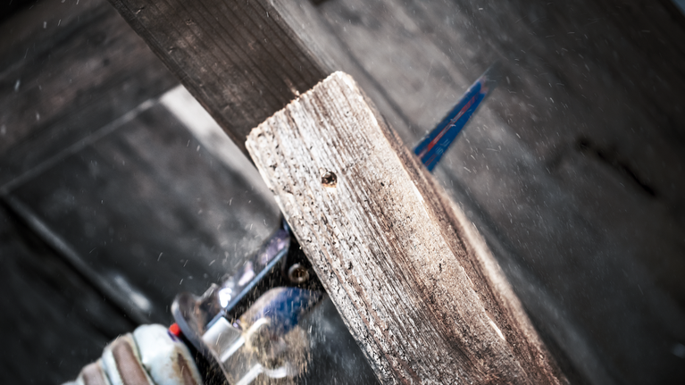 配戴安全設備的人員用往復鋸切割木板。