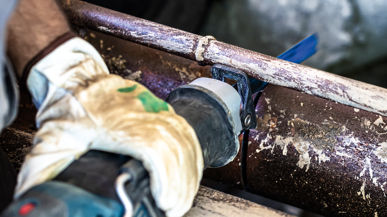 一名配戴安全設備的人用往復鋸切割生鏽的金屬管。