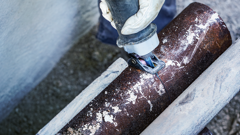 一名配戴安全設備的人用往復鋸切割生鏽的金屬管。