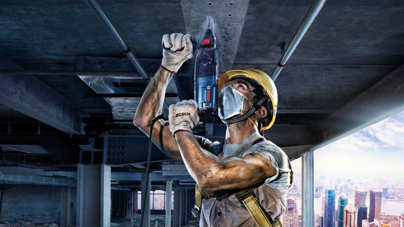 一名佩戴安全設備的人員在建築工地的混凝土天花板上鑽孔。.