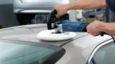 一個人在室內車庫裡用電動拋光機拋光汽車車頂。