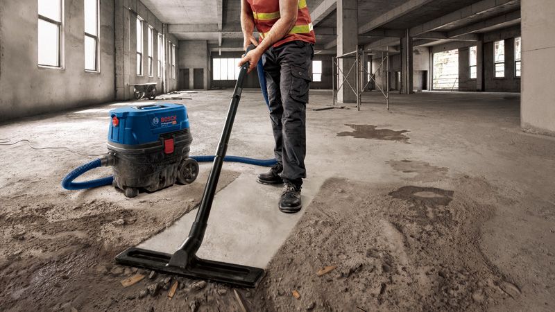 一名配戴安全設備的人員正在一棟未完工的大型建築物內吸塵混凝土灰塵。.