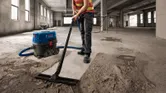 一名配戴安全設備的人員正在一棟未完工的大型建築物內吸塵混凝土灰塵。.