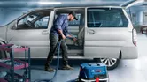 一名工人在車庫裡的工具車旁用吸塵器清潔汽車內部。.