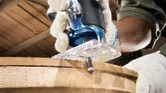 一名佩戴安全設備的人員使用手持銑刀修整木板的邊緣。.