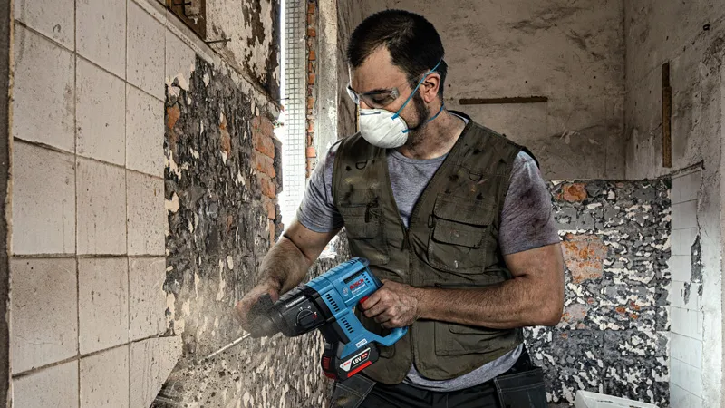 一名佩戴安全設備的人員使用電動工具從牆上拆除瓷磚。.