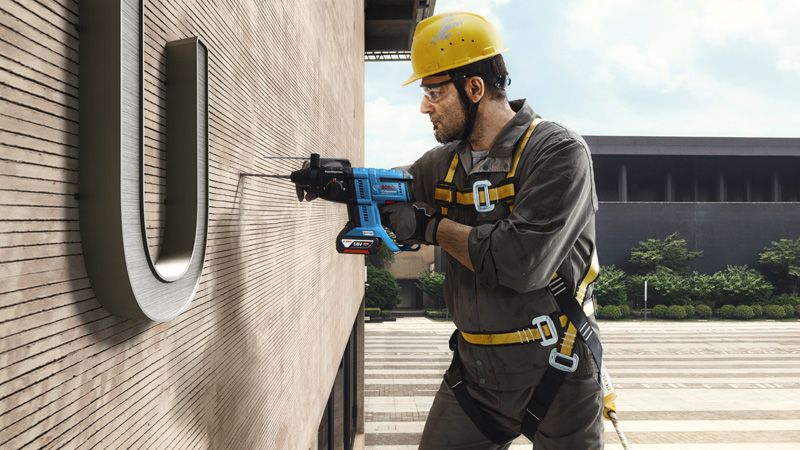 一名配戴安全設備的人員懸空鑽入建築物牆壁。.