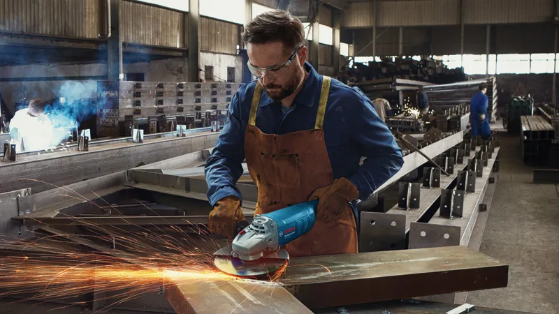 工廠裡，一名配戴安全設備的人員正在研磨金屬，產生火花。.