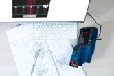 Detector device connected to a computer beside building plans and a keyboard.