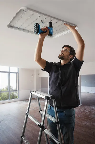 一名配戴安全設備的人員使用電鑽安裝天花板燈具。.