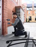 一名配戴安全設備的人員正在向建築物外牆的磚牆上鑽孔。