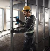 一名佩戴安全設備的人員正在鑽入正在建造的建築物的金屬螺柱。