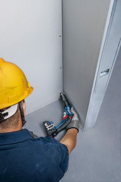 一名配戴安全設備的人員正在用無線螺絲起子固定乾牆。.