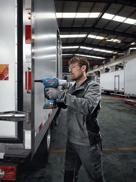 一名佩戴安全設備的工人使用無線電鑽將金屬固定在拖車上。.