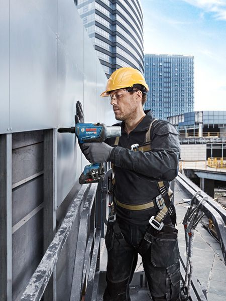 配戴安全設備的人員正在鑽入建築物外部的金屬面板。.