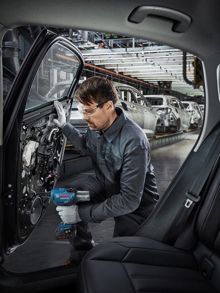 在汽車工廠裡，一名配戴安全設備的人員使用電動工具組裝車門。