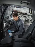 在汽車工廠裡，一名配戴安全設備的人員使用電動工具組裝車門。