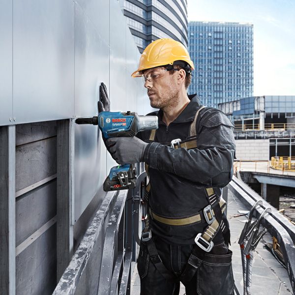 一名佩戴安全設備的人員使用電鑽將面板固定在建築物外部。.