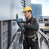 一名佩戴安全設備的人員使用電鑽將面板固定在建築物外部。