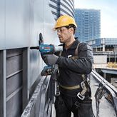 一名佩戴安全設備的人員使用電鑽將面板固定在建築物外部。.