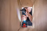 一名配戴安全設備的人員使用無線電鑽將螺絲旋入木製框架內。.