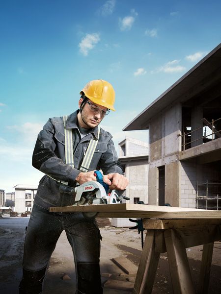 一名穿戴安全裝備的工人正在建築工地用圓鋸切割木材。