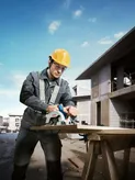 一名穿戴安全裝備的工人正在建築工地用圓鋸切割木材。