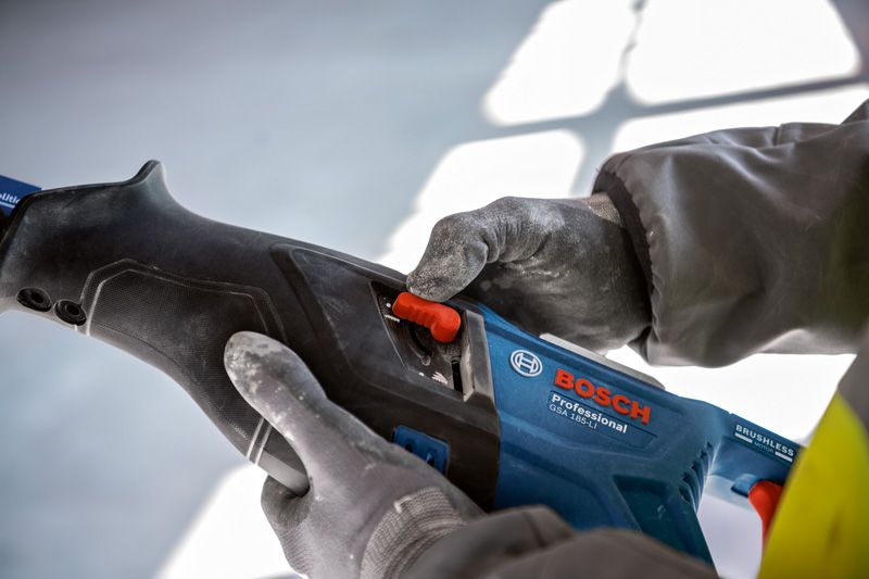 Person wearing safety equipment adjusts a power tool with a red switch.