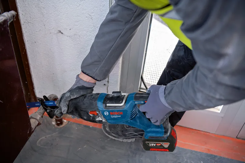 一名配戴安全設備的人員使用往復鋸切割門框附近的金屬。.