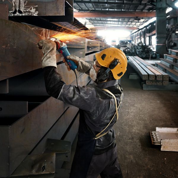A person wearing safety equipment grinds a metal beam, creating bright sparks.