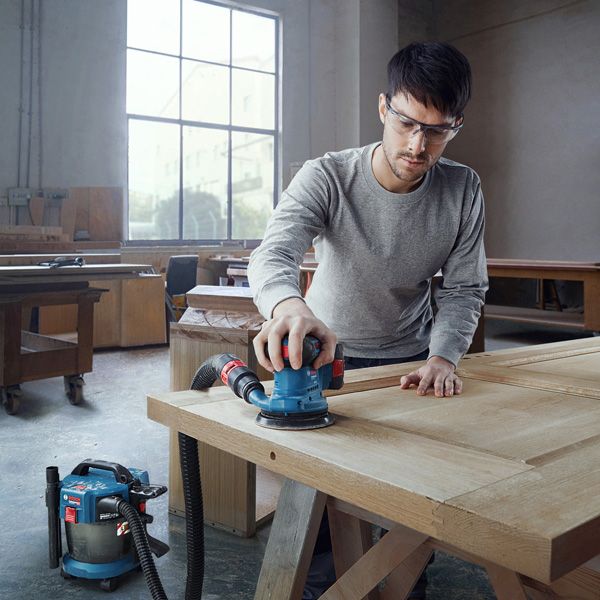 一名配戴安全設備的人員正在使用連接的軌道砂光機打磨木門。.