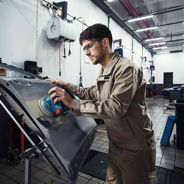 一名配戴安全設備的人員正在用電動砂光機打磨車門。.