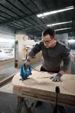 Person wearing safety equipment uses a jigsaw to cut curved shapes in plywood.