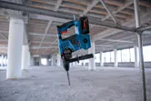 Cordless rotary hammer hanging on a metal pipe at an unfinished construction site.