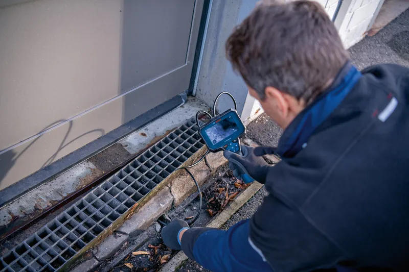 A person wearing safety equipment inspects a drain with an inspection camera.