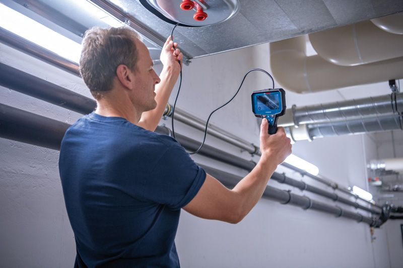 Person using an inspection camera to examine inside an overhead duct.
