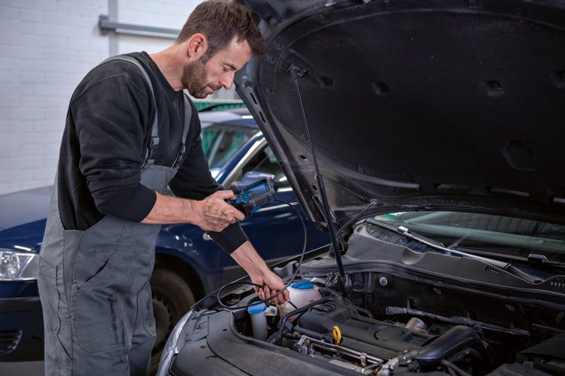 A person inspects a car engine with an inspection camera in a garage.