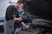 A person inspects a car engine with an inspection camera in a garage.