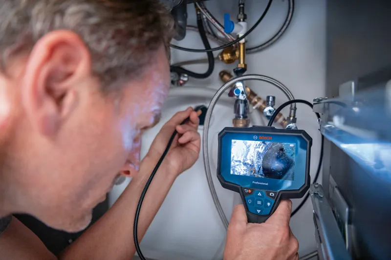 A person examines pipes under a sink using an inspection camera.