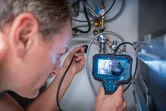 A person examines pipes under a sink using an inspection camera.